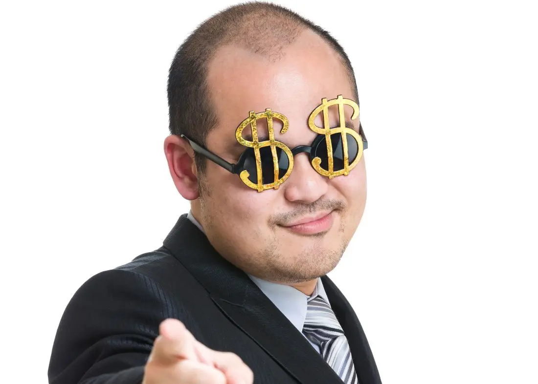 Over confident man in suit points smugly at camera, wearing dark glasses adorned with large gold dollar signs.